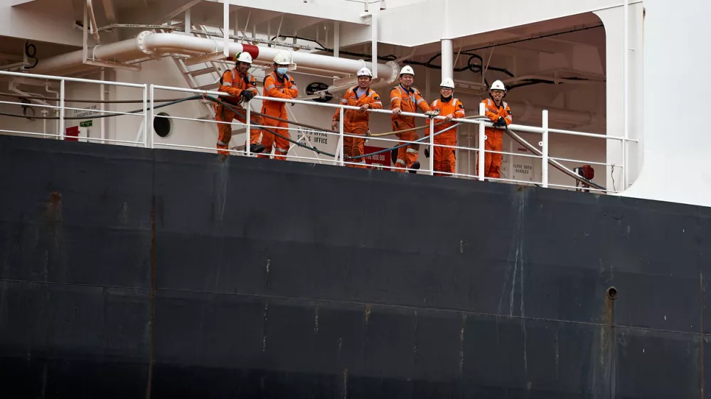 Six ship crew members wearing orange safety jumpsuits and hard hats posing together on the deck of a large vessel, Port of Gdansk, Pomerania, Poland, Europe. / Foto: Sebastian Gora Getty Images