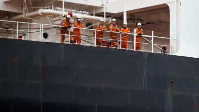 Six ship crew members wearing orange safety jumpsuits and hard hats posing together on the deck of a large vessel, Port of Gdansk, Pomerania, Poland, Europe. / Foto: Sebastian Gora Getty Images
