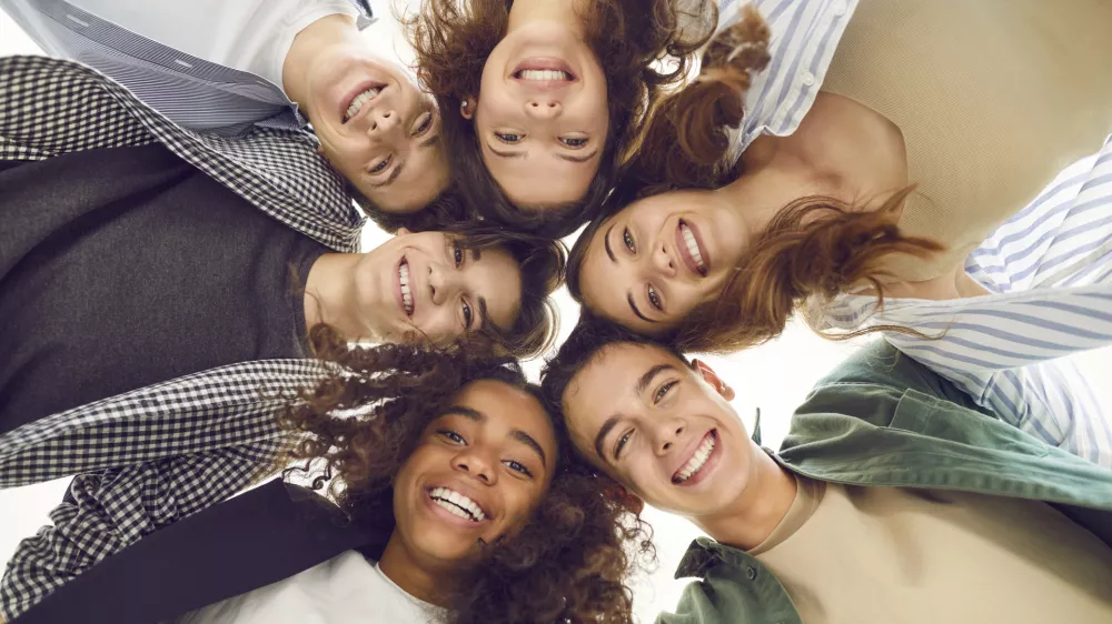 Group of diverse teenage students forms a circle, radiating togetherness and unity. They stand together, smiling at the camera, capturing harmonious school community and the spirit of teamwork. / Foto: Lacheev