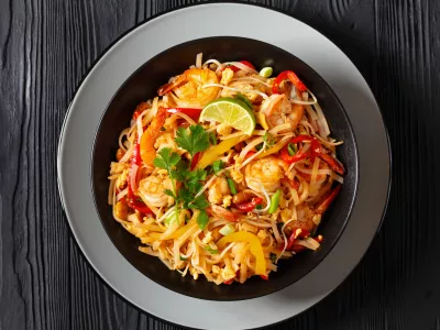 pad thai, phad thai, stir-fried rice noodles with shrimps, peanuts, scrambled eggs, bean sprouts, spring onion, red pepper, lime, in black bowl on black table, free space, flat lay, close-up / Foto: From_my_point_of_view