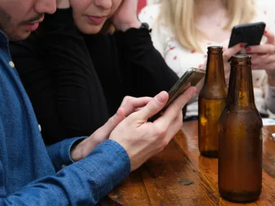 Unrecognizable three friends seeing something on their smartphone, drinking in a pub. Friendship concept. / Foto: Ladanifer Getty Images