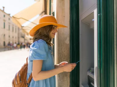 Beautiful girl taking the money from the ATM machine at her vacation.