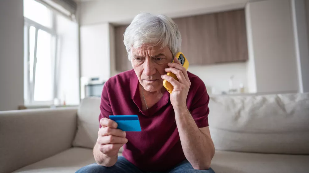Naive elderly pensioner trusting sharing card number with scammers on phone. Identity theft, card fraud, manipulation, financial deception, personal data exposure, phone scam, dishonest schemes