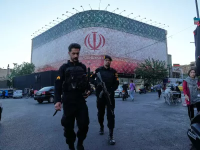 Policemen walk in front of a huge banner showing Iranian flag at the Islamic Revolution square in Tehran, Iran, Sunday, June 14, 2026. (AP Photo/Vahid Salemi)