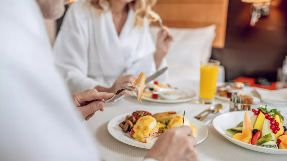 Breakfast time. A couple in white robes having breakfast and looking pleased / Foto: Oleksandr But Getty Images