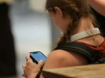 A teenager looks at her mobile phone in London, Monday, June 15, 2026. (AP Photo/Kin Cheung)