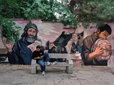 A man works on his smart phone in front of a mural honoring schoolchildren killed in a Feb. 28 strike in the southern Iranian city of Minab that was likely caused by U.S. airstrikes, in northern Tehran, Monday, June 15, 2026. (AP Photo/Vahid Salemi)