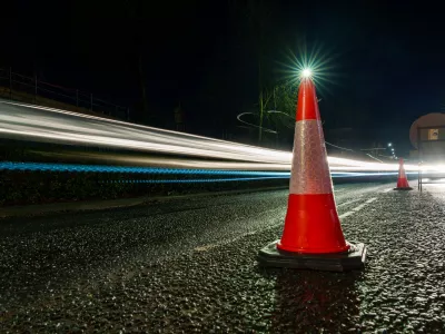 Traffic cone on a road at night with light trails from passing vehicles.