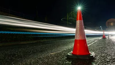 Traffic cone on a road at night with light trails from passing vehicles.