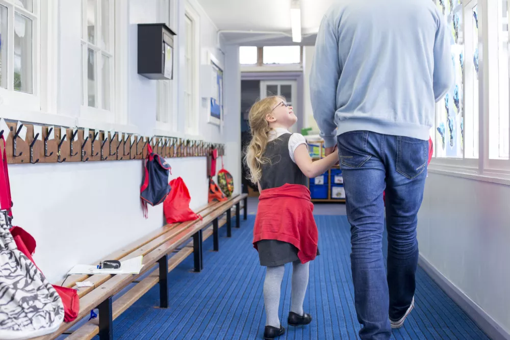 Little girl walking through her nursery corridor with her father. She is holding his hand and looking up to him with a smile on her face. / Foto: Dglimages Getty Images/istockphoto