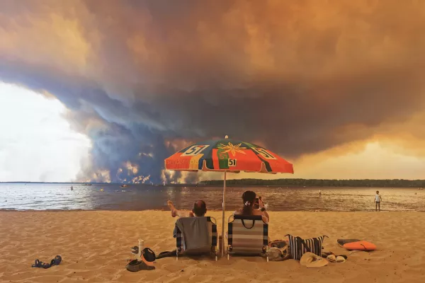 Beach goers rest on the beach of Moutchic on the shore of Lake Lacanau (Etang de Lacanau) in Lacanau, southwestern France on July 24, 2026, as clouds of smoke rise into the sky from the Gironde wildfire. The fire raging in the northern part of the Arcachon Basin in Gironde, southwest France, has swept through more than 3,400 hectares, according to the latest figures released by the prefecture. More than 20,000 residents and tourists have been evacuated from this part already devastated by flames in 2022. Scientists have long warned that climate change caused by human use of fossil fuels will make periods of drought more intense and longer-lasting, creating the ideal conditions for wildfires.,Image: 1118260144, License: Rights-managed, Restrictions:, Model Release: no / Foto: Profimedia
