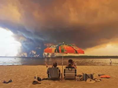 Beach goers rest on the beach of Moutchic on the shore of Lake Lacanau (Etang de Lacanau) in Lacanau, southwestern France on July 24, 2026, as clouds of smoke rise into the sky from the Gironde wildfire. The fire raging in the northern part of the Arcachon Basin in Gironde, southwest France, has swept through more than 3,400 hectares, according to the latest figures released by the prefecture. More than 20,000 residents and tourists have been evacuated from this part already devastated by flames in 2022. Scientists have long warned that climate change caused by human use of fossil fuels will make periods of drought more intense and longer-lasting, creating the ideal conditions for wildfires.,Image: 1118260144, License: Rights-managed, Restrictions:, Model Release: no / Foto: Profimedia