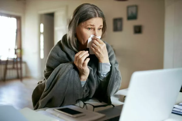 Sick elderly woman wrapped in plaid coughing, sneezing, having respiratory disease symptoms, sitting in front of open laptop, having online video consultation with her physician. Health and technology / Foto: Shurkin_son