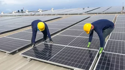Male team workers in protective helmet installing solar photovoltaic panel system using screwdriver. Electrician mounting blue solar module on roof of modern house.