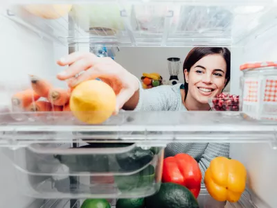 Smiling woman taking a fresh lemon out of the fridge, healthy food concept
