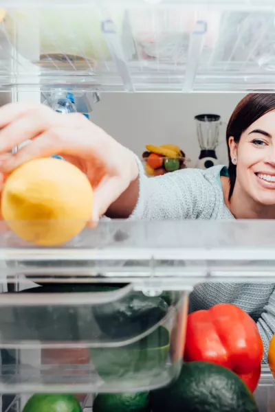 Smiling woman taking a fresh lemon out of the fridge, healthy food concept