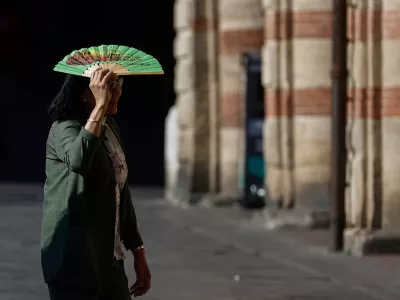 A woman holds a fan over her face to shield herself from the sun during hot weather in Bologna, Italy, June 20, 2026. REUTERS/Vincenzo Livieri