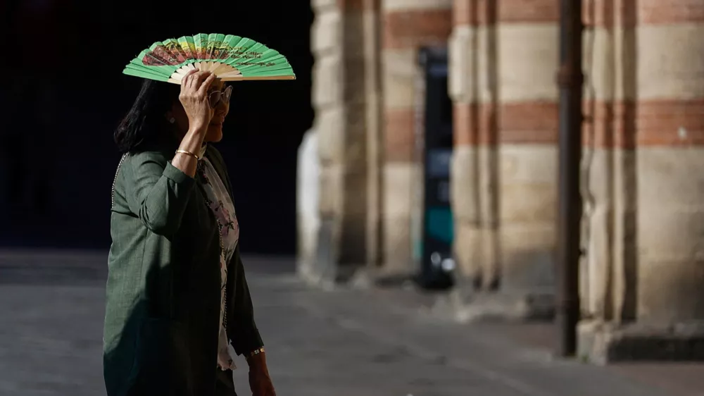 A woman holds a fan over her face to shield herself from the sun during hot weather in Bologna, Italy, June 20, 2026. REUTERS/Vincenzo Livieri