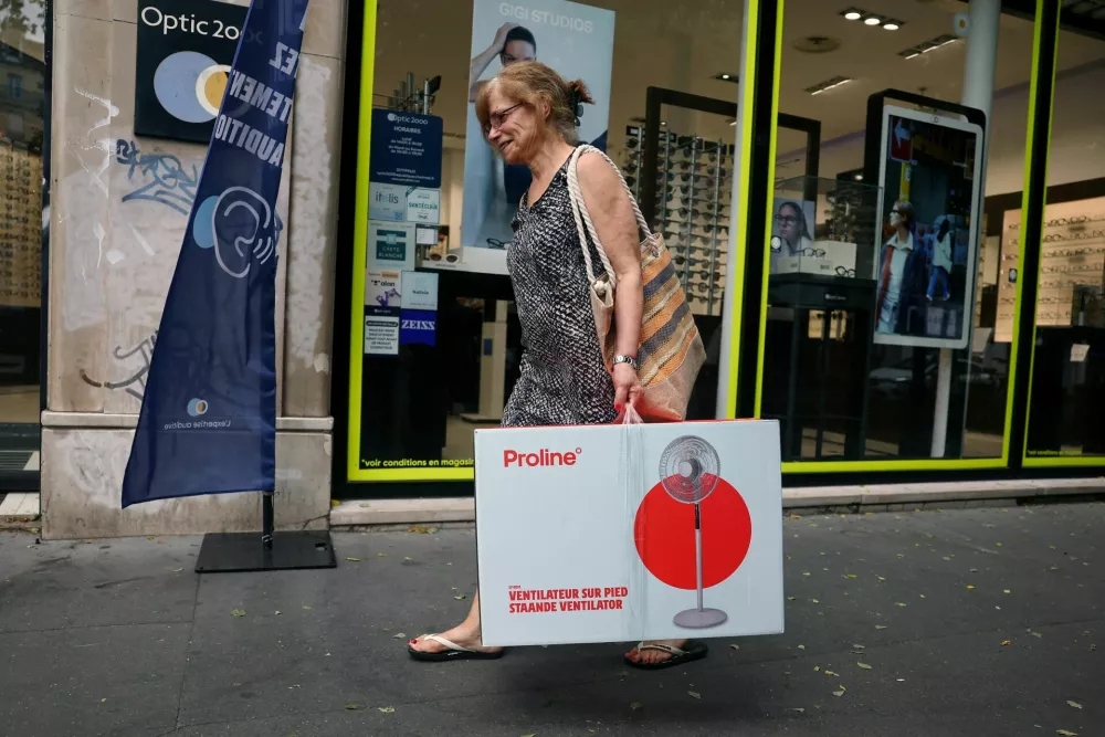 A woman carrying an electric fan in a cardboard box walks down a street as temperatures rise in Paris during a heatwave affecting a large part of France, June 23, 2026. REUTERS/Abdul Saboor
