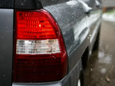 Red taillight of a gray car glows while snowflakes fall against the wet bodywork. Shallow depth of field and droplets highlight movement safety and winter driving atmosphere.,Image: 1093484948, License: Royalty-free, Restrictions:, Model Release: no 