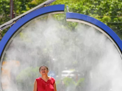 A woman cools off in a water mist machine installed by city administration to assist people in coping with the heat on a torrid day, as the National Weather forecaster issued an extreme heat code red warning for most parts of the country, in Bucharest, Romania, Monday, June 29, 2026. (AP Photo/Vadim Ghirda)