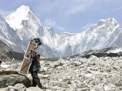 FILE - In this Friday, April 10, 2015, file photo, a porter carries crates containing oxygen tanks, with Mt Lingtren seen behind left, and Mt. Khumbutse, right, on his way towards Everest Base Camp, at Lobuche, Nepal. A Nepalese official says Sherpa workers are fixing the final route to the summit of Mount Everest and the first climb of the season could be days away. (AP Photo/Tashi Sherpa, File)