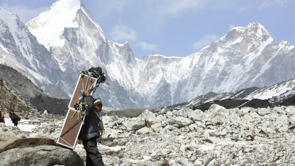 FILE - In this Friday, April 10, 2015, file photo, a porter carries crates containing oxygen tanks, with Mt Lingtren seen behind left, and Mt. Khumbutse, right, on his way towards Everest Base Camp, at Lobuche, Nepal. A Nepalese official says Sherpa workers are fixing the final route to the summit of Mount Everest and the first climb of the season could be days away. (AP Photo/Tashi Sherpa, File)