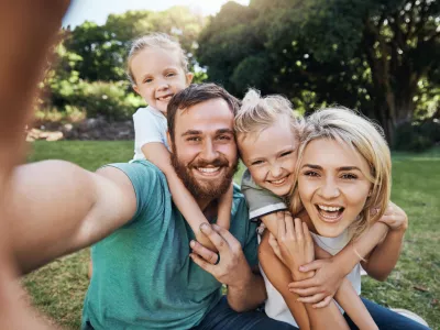 Nature, selfie and portrait of a happy family on a picnic together in outdoor green garden. Happy, smile and parents playing, hugging and bonding with children outside in backyard or park in canada.