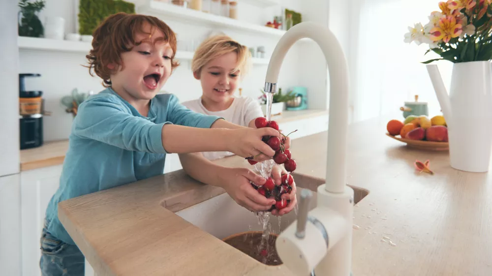 happy kids washing cherries under tap water at the kitchen