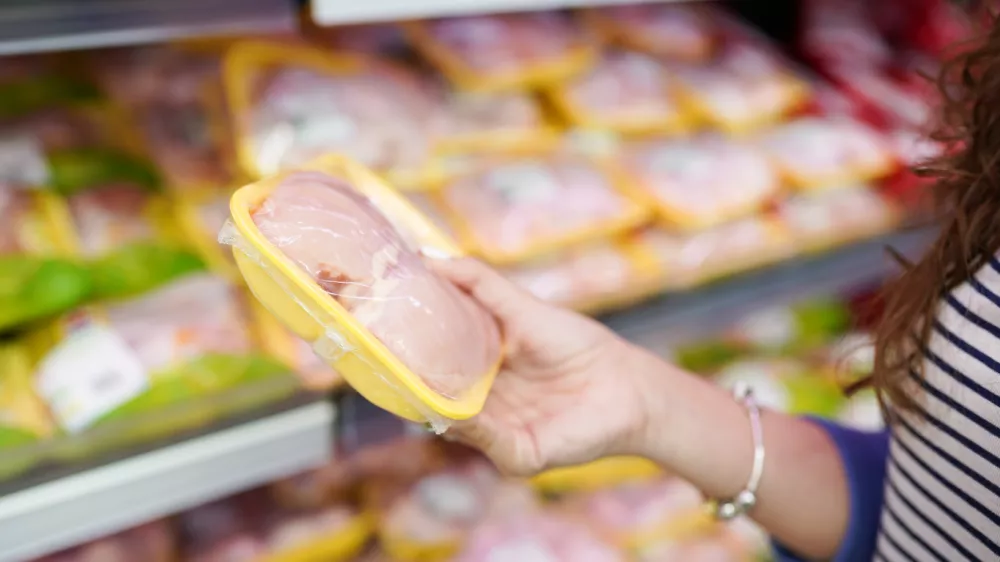 meat in food store. Woman choosing packed fresh chicken meat in supermarket.