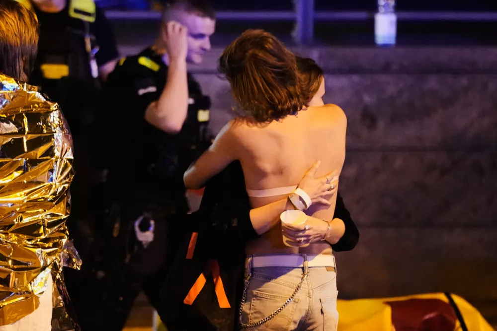 Two people embrace near others wearing thermal blankets as they stand near emergency personnel in Berlin, early Sunday, July 26, 2026, following the cancellation of Christopher Street Day festivities. (AP Photo/Markus Schreiber)