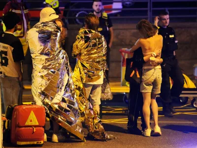 Two people embrace near others wearing thermal blankets as they stand near emergency personnel in Berlin, early Sunday, July 26, 2026, following the cancellation of Christopher Street Day festivities. (AP Photo/Markus Schreiber)