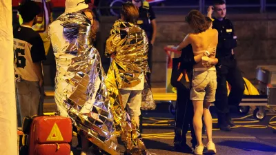 Two people embrace near others wearing thermal blankets as they stand near emergency personnel in Berlin, early Sunday, July 26, 2026, following the cancellation of Christopher Street Day festivities. (AP Photo/Markus Schreiber)