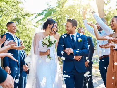 Wedding guests throwing rose petals confetti tradition over bride and groom on their special day. Newlywed couple walking past friends and family