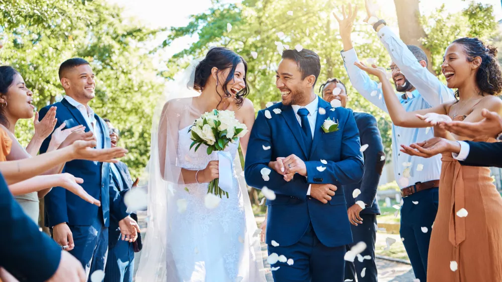 Wedding guests throwing rose petals confetti tradition over bride and groom on their special day. Newlywed couple walking past friends and family