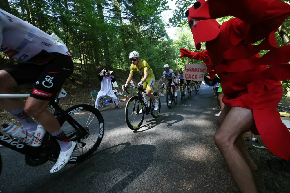 Cycling - Tour de France - Stage 9 - Malemort to Ussel - Malemort, France - July 12, 2026 UAE Team Emirates - XRG's Tadej Pogacar wearing the yellow jersey, UAE Team Emirates - XRG's Isaac Del Toro wearing the white jersey and Team Visma | Lease a Bike's Jonas Vingegaard wearing the polka-dot jersey in action as a spectator dressed in a costume cheers on during stage 9 REUTERS/Gonzalo Fuentes