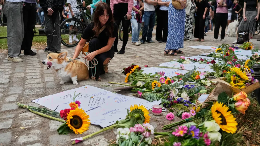 People stop by the memorial site commemorating the victims near the scene where a car rammed into a crowd at the Pride March in Berlin, Germany, Sunday, July 26, 2026. (AP Photo/Markus Schreiber)