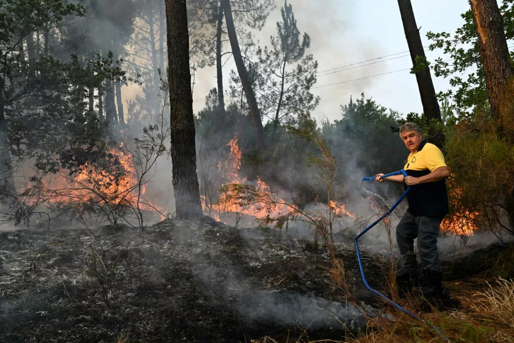 A local resident uses a hose to put out flames burning across the road from his house near Marcheprime, outside, Bordeaux, France, Sunday, July 26, 2026. (AP Photo/Emma Da Silva)