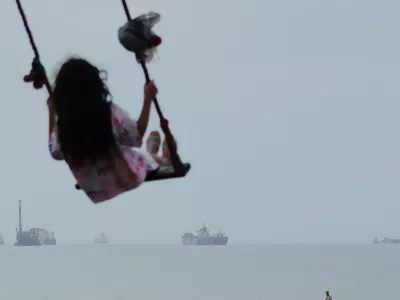 A girl swings along the shore as cargo ships and other commercial vessels appear anchored in the Strait of Hormuz off Bandar Abbas, Iran, Monday, July 27, 2026. (Razieh Poudat/ISNA via AP) / Foto: Razieh Poudat
