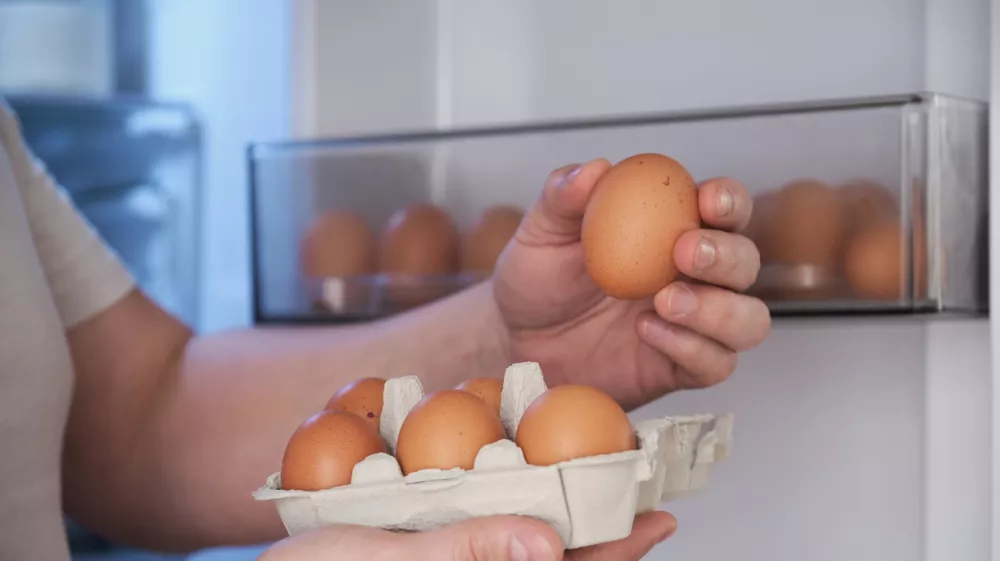 Close up of a man putting fresh eggs into refrigerator.