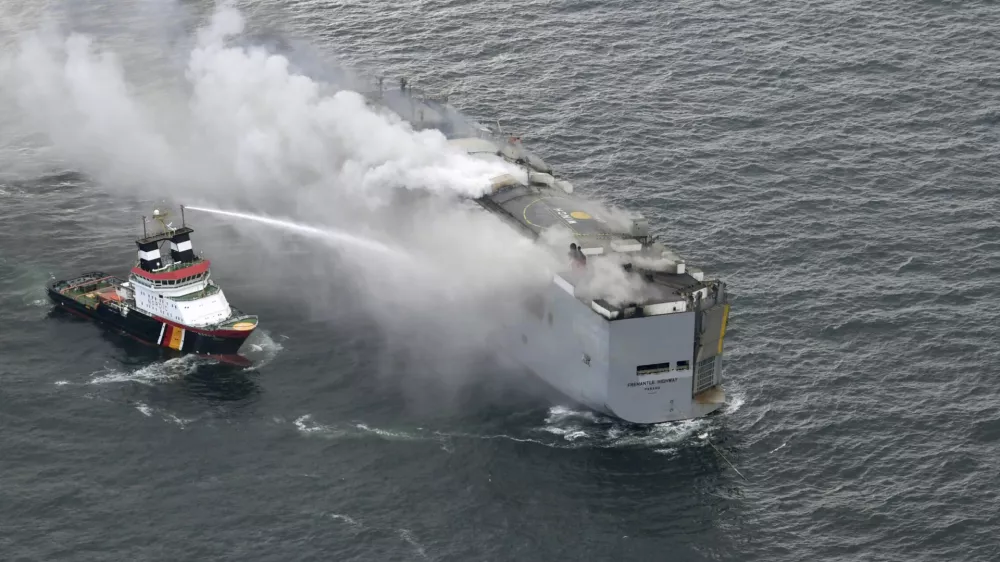 A boat hoses the smoke from a fire which broke out on a freight ship in the North Sea, about 27 kilometers (17 miles) north of the Dutch island of Ameland, Wednesday, July 26, 2023. A fire on the freight ship Fremantle Highway, carrying nearly 3,000 cars, was burning out of control Wednesday in the North Sea, and the Dutch coast guard said it was working to save the vessel from sinking close to an important habitat for migratory birds. (Kustwacht Nederland/Coast Guard Netherlands via AP)