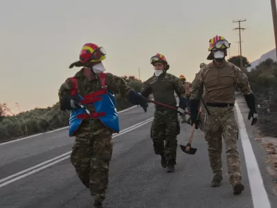 Firefighters walk along a road carrying firefighting tools during a wildfire in the Rethymno region on the southern Greek island of Crete, Wednesday, July 29, 2026, where two firefighters died while battling the blaze. (AP Photo/Giannis Angelakis)