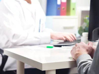 Doctor and patient in appointment, visit or meeting in hospital office or emergency room. Physician or nurse writing prescription, instructions, medical record or data with computer.
