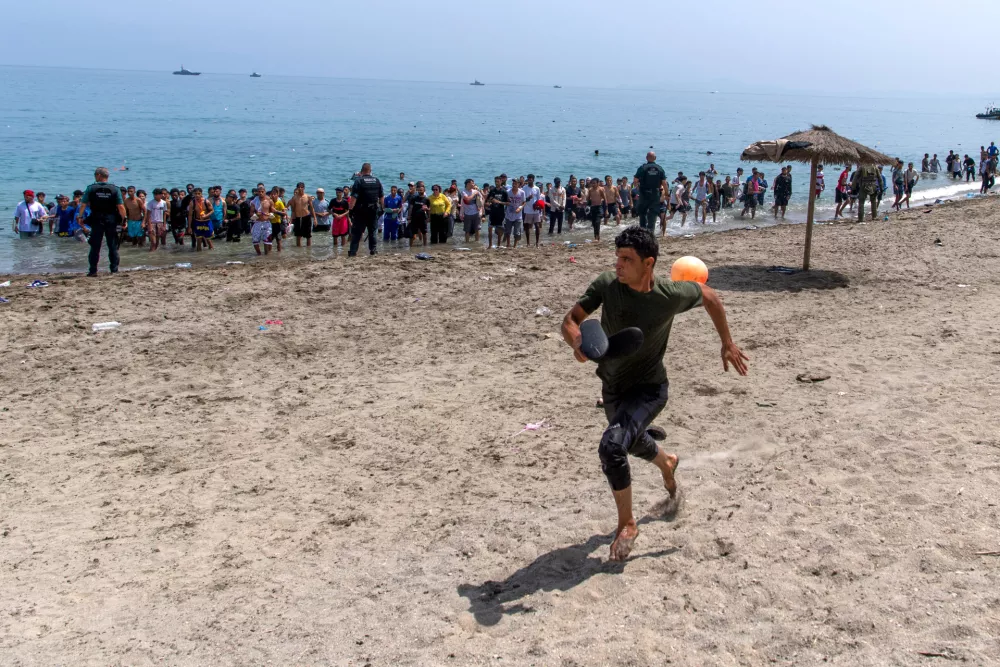 A migrant runs from Spanish police officers as they cordon off access to the beach for people crossing from Morocco into the Spanish enclave of Ceuta, Friday, July 31, 2026. (AP Photo/Antonio Sempere)
