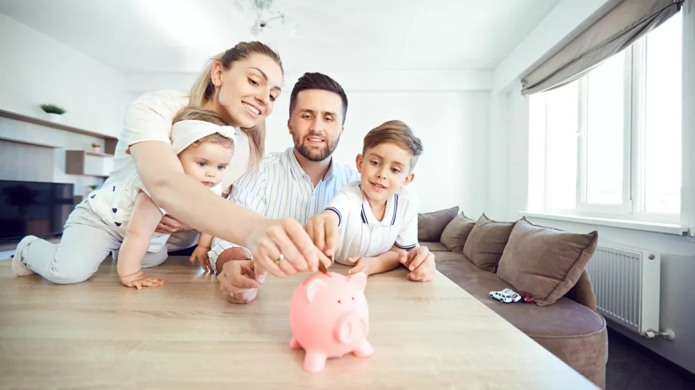 A smiling family saves money with a piggy bank. Happy family at the table in the room.