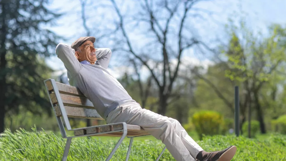 Elderly man relaxing on a park bench on a sunny day / Foto: Ljupco