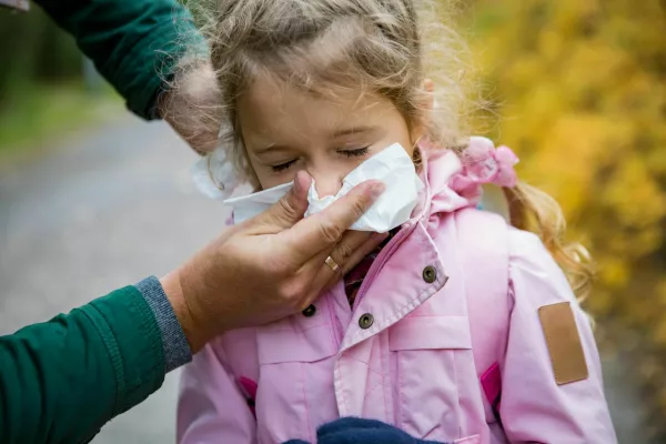 Father wiping daughter's nose with handkerchief. Sick little girl with cold and flu standing outdoors. Preschooler sneezing, coughing, having runny red nose. Autumn street background / Foto: Suzi Media Production