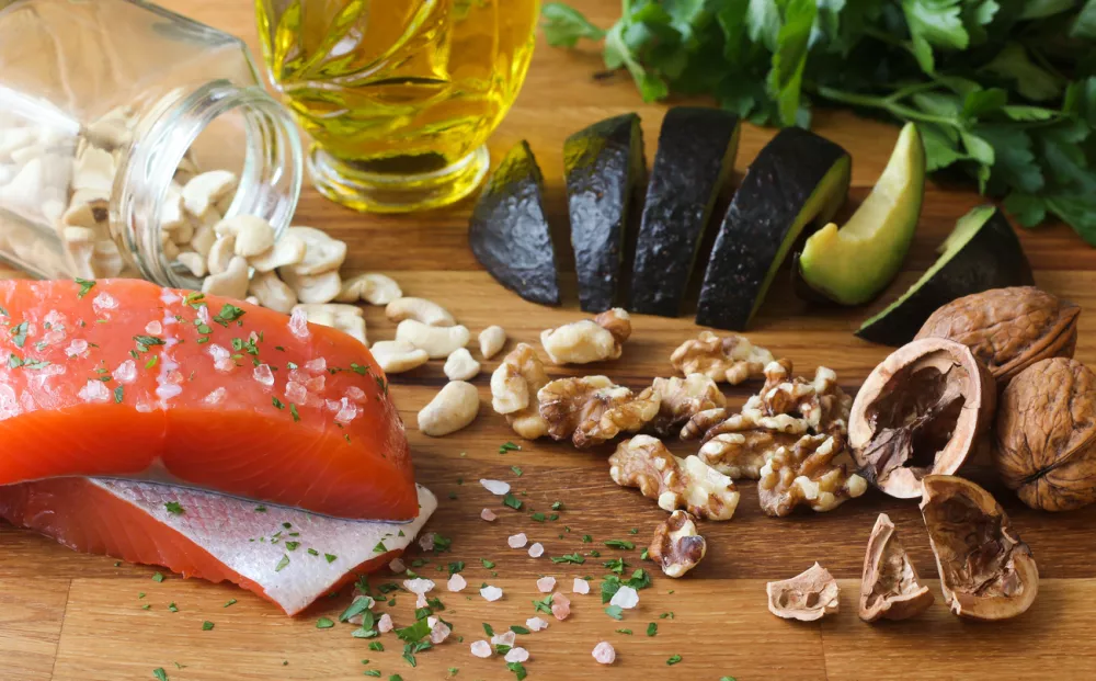Salmon seasoned with salt, cashews, walnuts, sliced avocado, and olive oil on a butcher block, garnished with parsley. / Foto: Autumnhoverter Getty Images