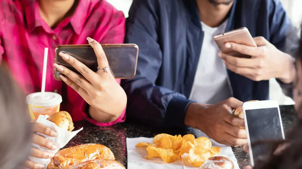 Group of unrecognizable people busy on mobile while having snacks together at restaurant - Concept of millennials having junk food, phone addiction, social media sharing and connection