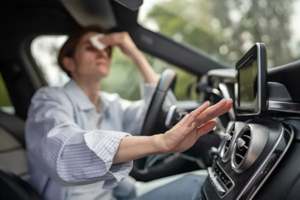 Woman drives car with broken air conditioning in hot summer weather wipes sweat on forehead with paper napkin. Middle aged female suffering from heat stuffiness. Exhausted overheated stressed driver.